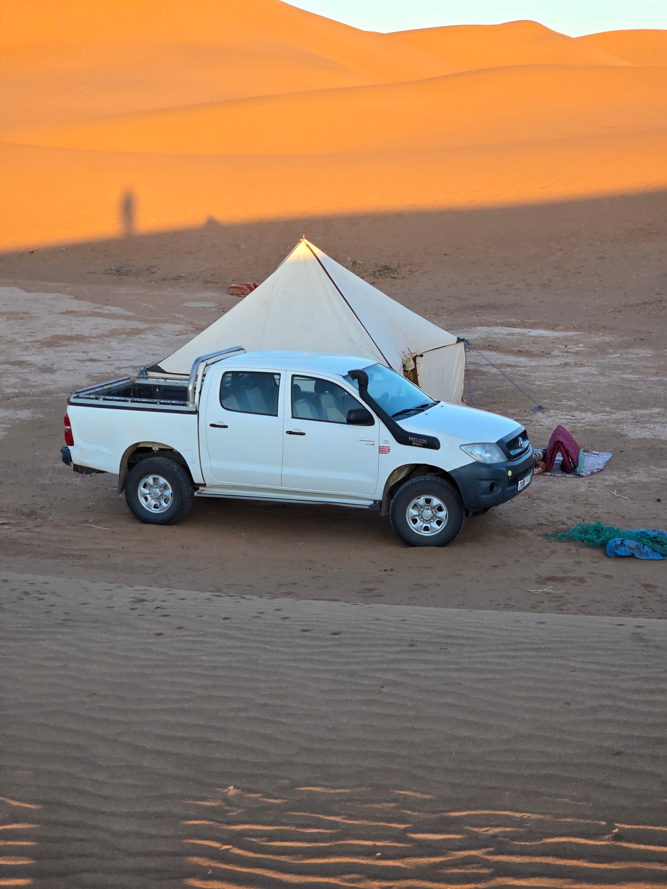 White 4x4 vehicle parked beside a desert tent below orange dunes.