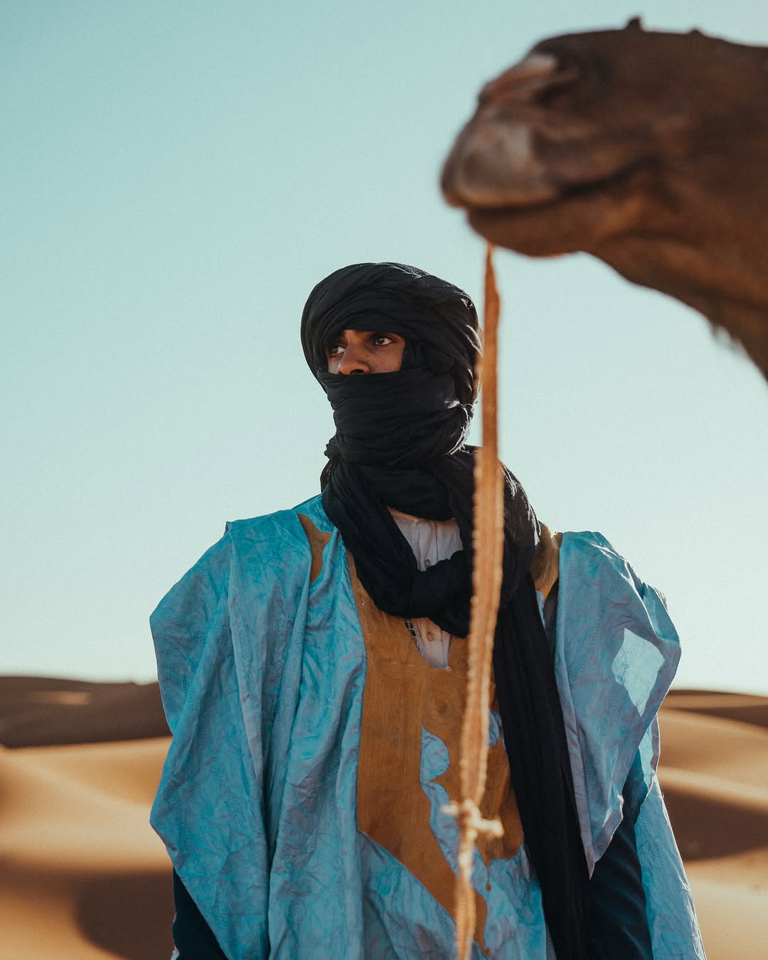 Ali El Gasmi, founder and desert guide of Sahara Caravan, standing in the Sahara with a camel.