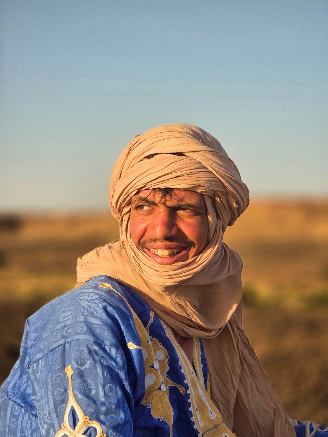Ossama, smiling camel guide, in a blue desert robe and pale turban.